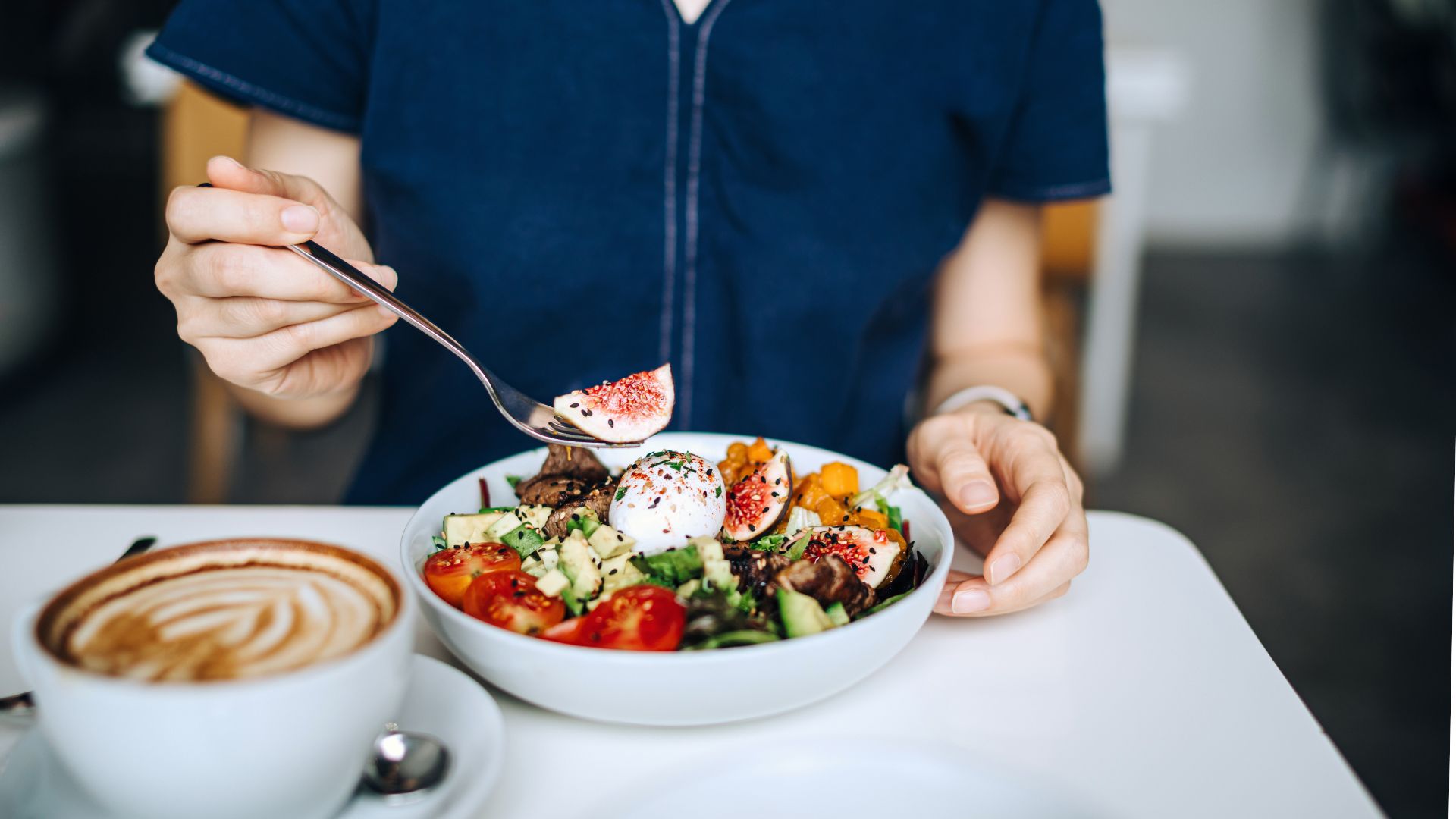 woman having a dish of fresh beef cobb salad with a cup of coffee at a cafe table