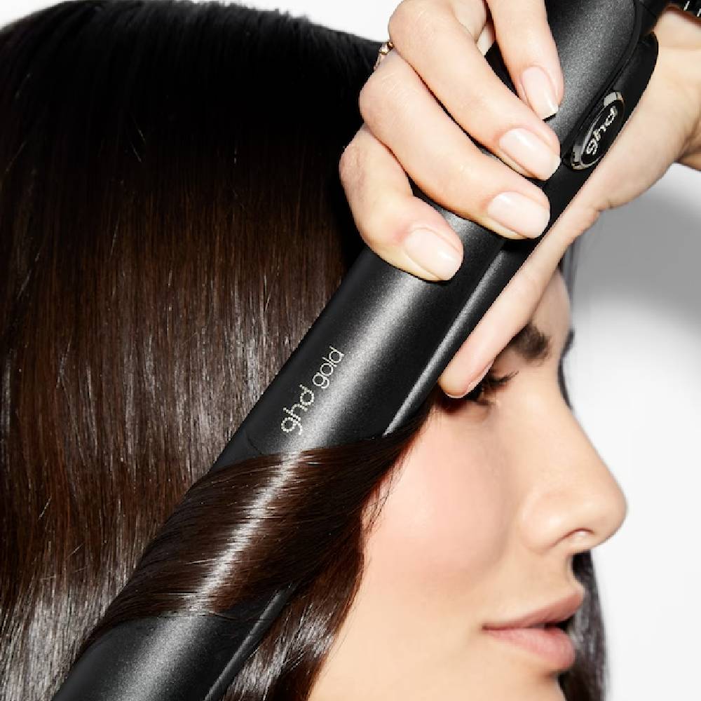 A close up of a woman using a ghd straightener.