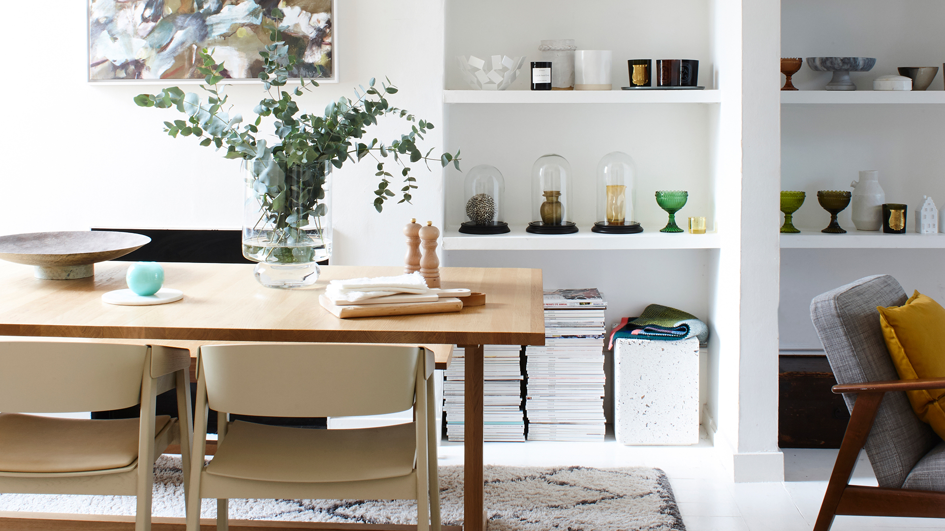 white dining room with wooden dining table with alcove shelving used to store stacked magazines and glassware