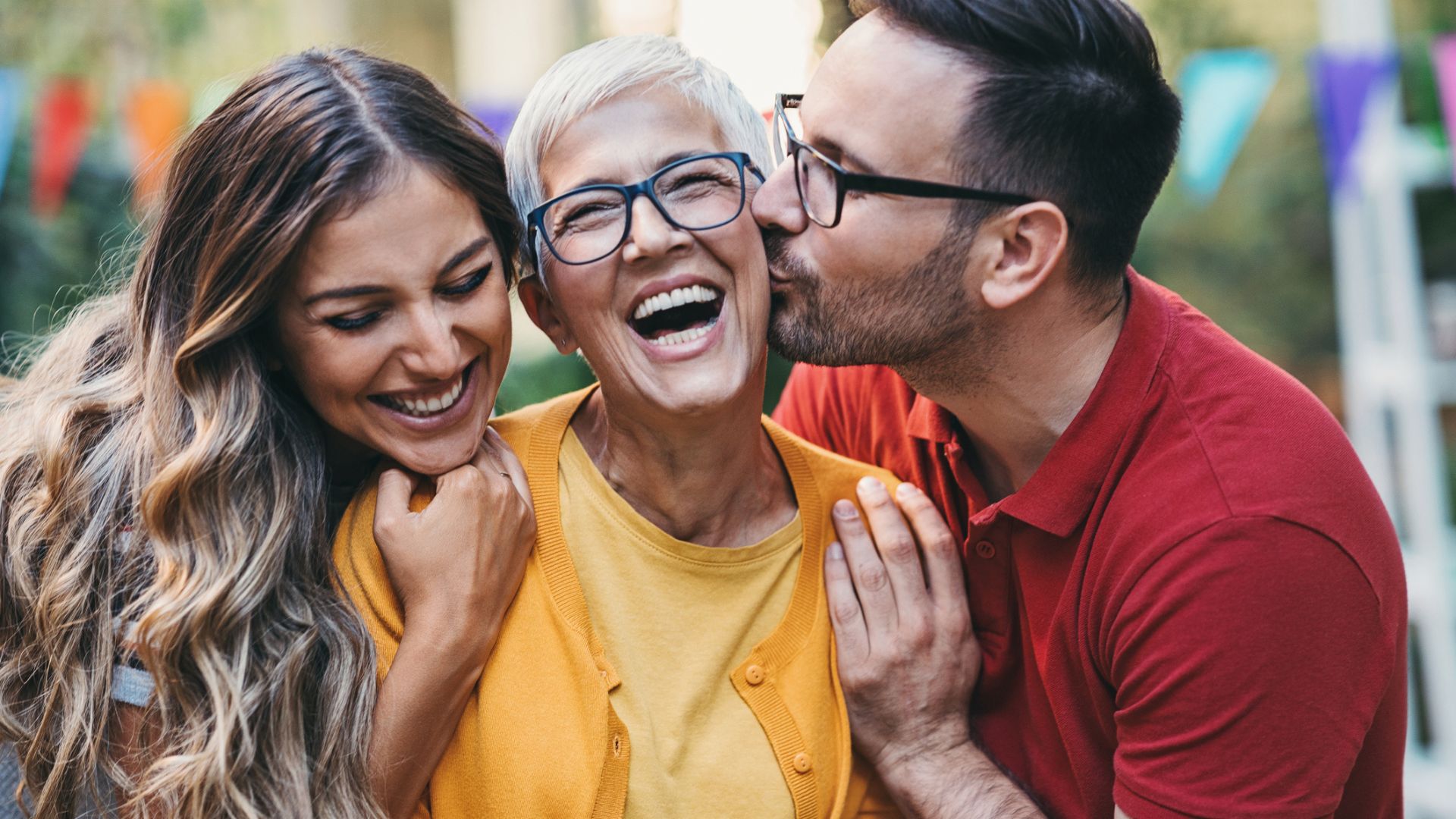 A glamorous, laughing woman is embraced by an adult son and daughter